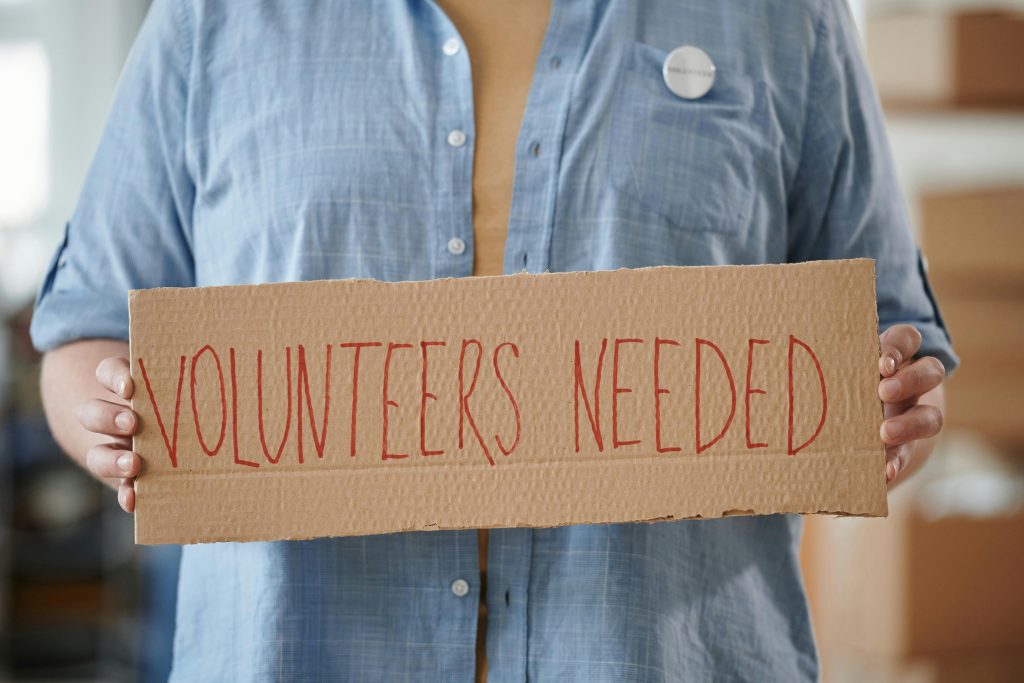 a man holding sign reading volunteers needed
